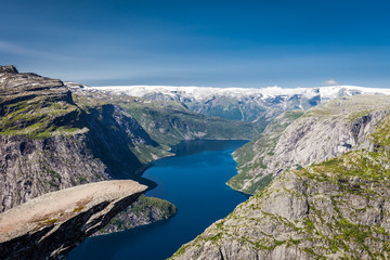 Panoramic view of empty Trolltunga cliff, Norway, Scandinavia. Sunny day with amazing blue sky. Majestic mountains in the background. Clear blue water. 