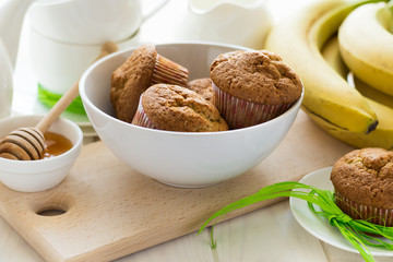 Tea time: homemade banana muffins, honey, bananas and tea settings on white wooden table. Selective focus