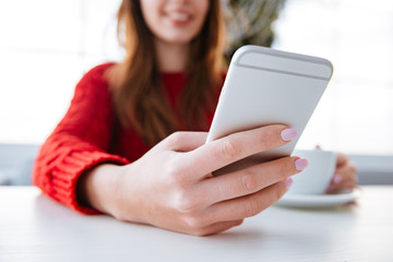 Closeup of woman using smartphone and drinking coffee in cafe