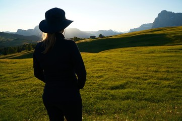 Wanderin genießt Morgensonne und Aussicht auf Wiese und Berge in Südtirol / Seiser Alm / Gröden