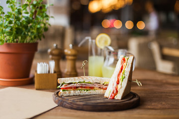Appetizing sandwich with ham, tomato, lettuce, cheese on the wooden plate in the restaurant