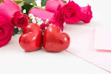 Two red hearts with pink envelope and red roses closeup.