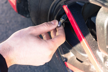 Man opening valve tire cap of car wheel
