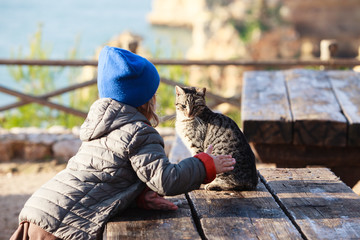 Adorable little kid playing with striped cat 

