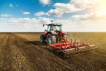 Farmer in tractor preparing land with seedbed cultivator as part of pre seeding activities in early spring season of agricultural works at farmlands. - obrazy, fototapety, plakaty