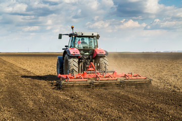 Fototapeta premium Farmer in tractor preparing land with seedbed cultivator as part of pre seeding activities in early spring season of agricultural works at farmlands.