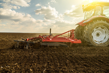 Farmer in tractor preparing land with seedbed cultivator as part of pre seeding activities in early spring season of agricultural works at farmlands.