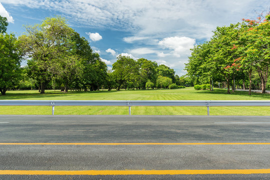 Side View Of Asphalt Road With Green Grass Field In Park