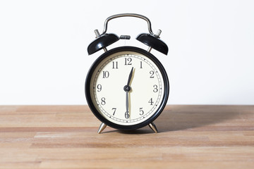 It is half past twelve o'clock. The time is 12:30. Retro clock isolated on a wooden table. White background.