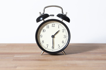 It is half past one o'clock. The time is 1:30. Retro clock isolated on a wooden table. White background.