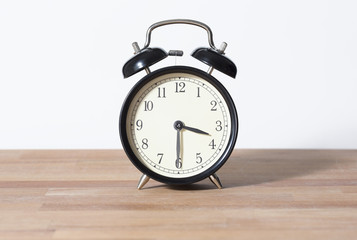 It is half past three o'clock. The time is 3:30. Retro clock isolated on a wooden table. White background.