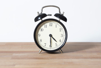 It is half past four o'clock. The time is 4:30. Retro clock isolated on a wooden table. White background.