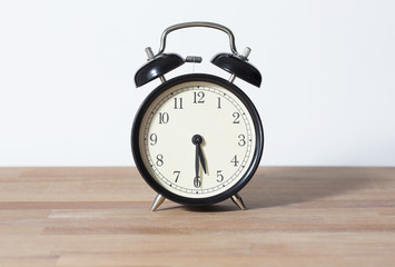 It is half past five o'clock. The time is 5:30. Retro clock isolated on a wooden table. White background.