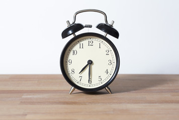 It is half past seven o'clock. The time is 7:30. Retro clock isolated on a wooden table. White background.