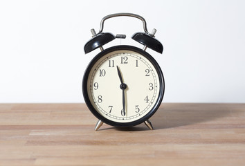 It is half past eleven o'clock. The time is 11:30 am or pm. Retro clock isolated on a wooden table. White background.