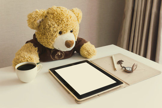 Cute bear doll watching taplet on table