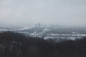 Nice winter landscape. Morning in city. Metro bridge connects the two banks of the city. Road goes for horizon. Buildings are hiding in the fog on the left bank of the Dnipro. Kyiv. Ukraine