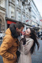 Beautiful young couple in love enjoying together at city street, kissing and holding together a lollipop in heart shape. 