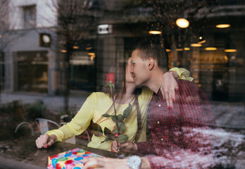 Beautiful young couple in love enjoying together at cafeteria, and man is giving a gift as surprise to his girlfriend. 