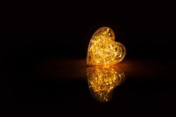 Warm glowing orange heart with reflection on dark black background