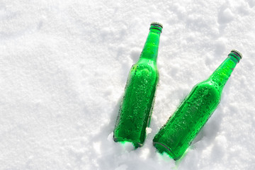 Two bottles of cold beer on the snow at sunset. Close up view.