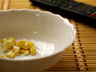 last popcorn in a white bowl and tv remote, shallow depth of field, selective focus