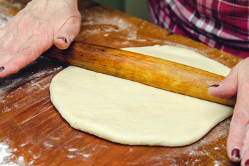 Rolling pin in hands, rolling dough on the wooden table, close-up.