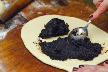 Process of making strudel pie, woman spoon puts poppy stuffing on the dough, wooden board.
