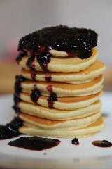 Homemade sweet pancakes with berry jam on a white plate, close up