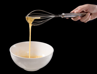 Wire whisk with eggs in bowl isolated on black background