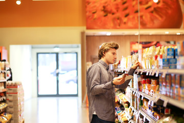  Man shopping in supermarket reading product information.Using smarthone
