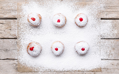 Fototapeta na wymiar Fresh donuts (sufgania) with red jelly jam on a sugar powder and wooden background. Hanukkah holiday celebration and traditional jewish sweet