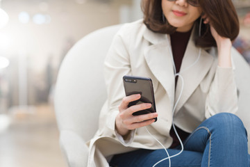 gorgeous woman in trench coat use smartphone listen via ear phon