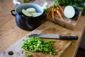 Sliced green onion stems on wooden cutting board, selective focus. Healthy vegetable in a background.