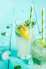 Selection of summer refreshing cocktails with mint (lemonade or mojito): with lemon, orange, lime. On light blue wooden table, bright sunlight. Copy space, close view