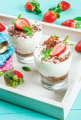     Summer dessert, classic cheesecake with strawberries decorated with mint leaves. On the tray on a light blue wooden table, bright sunlight. Copy space