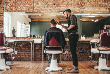 Hairstylist serving client at barber shop - obrazy, fototapety, plakaty