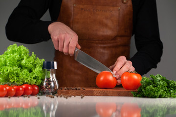 Man's hands cutting red fresh tomato on a wooden board