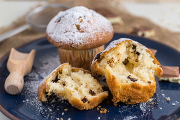 Muffins powdered by sugar on blue plate and white wooden background.