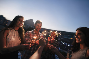 Friends enjoying rooftop party with sparklers - obrazy, fototapety, plakaty