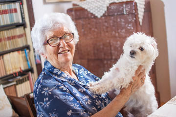 Happy elderly woman holding small Maltese dog.