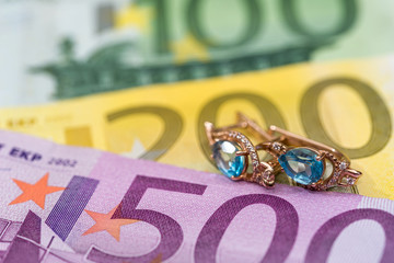 gold earrings lying on euros banknote.