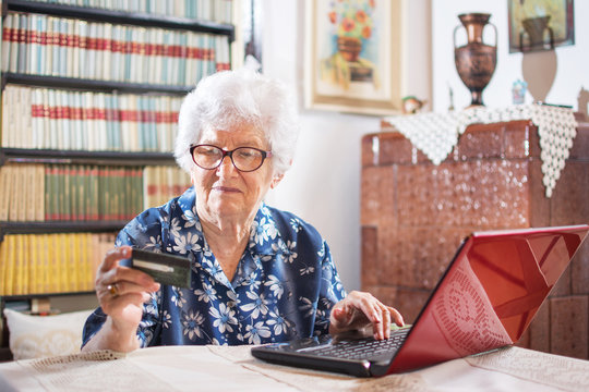 Old woman looking at credit card and typing its data to online form.