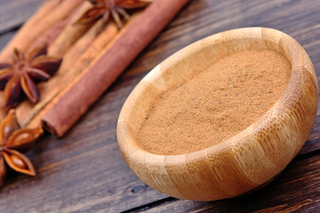 Cinnamon powder in a bowl with star anise and cinnamon sticks on table