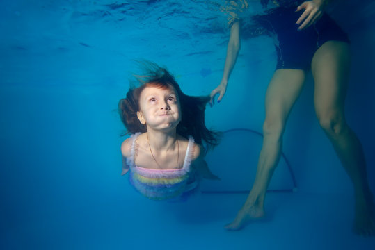 The little girl with the coach learning how to swim underwater in the pool. POPs up from the bottom and looking up. Portrait. Shooting under the water surface. Horizontal view
