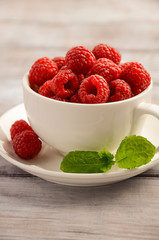 Ripe sweet raspberries in white cup on wooden table, selective focus, vertical, close up, copy space.