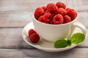 Ripe sweet raspberries in white cup on wooden table, selective focus, horizontal, close up, copy space.