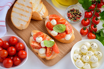 Bruschetta with cherry tomatoes and mozzarella on wooden board, top view