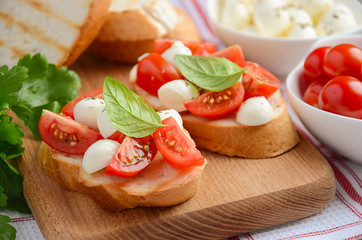 Bruschetta with cherry tomatoes and mozzarella on wooden board, selective focus, horizontal