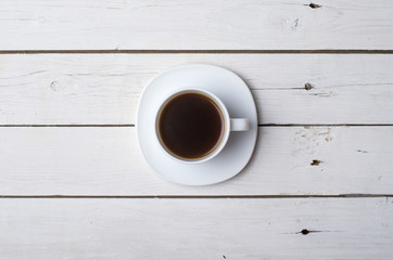 A cup of hot coffee on a white wooden table, top view.